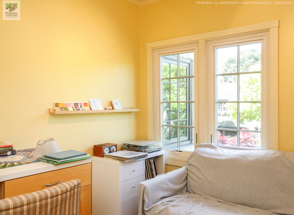 Foto på ett mellanstort arbetsrum, med gula väggar, mellanmörkt trägolv och ett fristående skrivbord