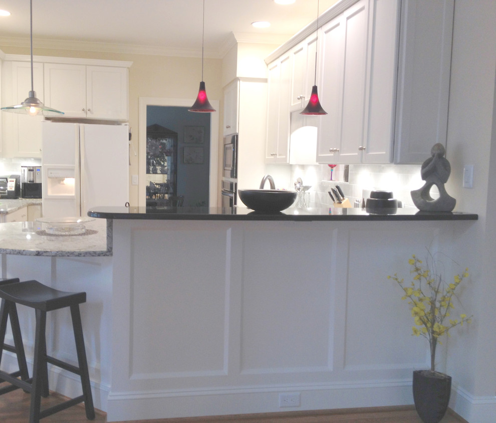 Mid-sized transitional l-shaped medium tone wood floor eat-in kitchen photo with an undermount sink, recessed-panel cabinets, white cabinets, granite countertops, white backsplash, stone tile backsplash, stainless steel appliances and a peninsula