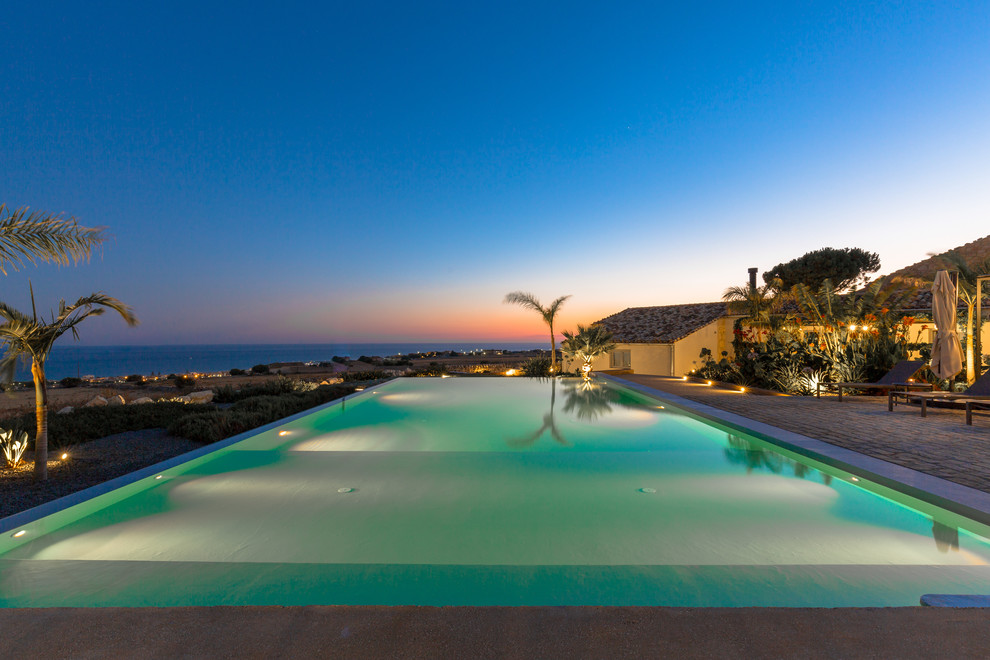 This is an example of a large beach style backyard rectangular infinity pool in Other.