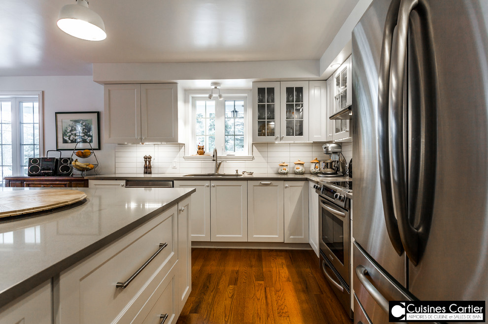 Inspiration for a large transitional medium tone wood floor eat-in kitchen remodel in Montreal with a double-bowl sink, shaker cabinets, white cabinets, quartzite countertops, white backsplash, ceramic backsplash, stainless steel appliances and an island