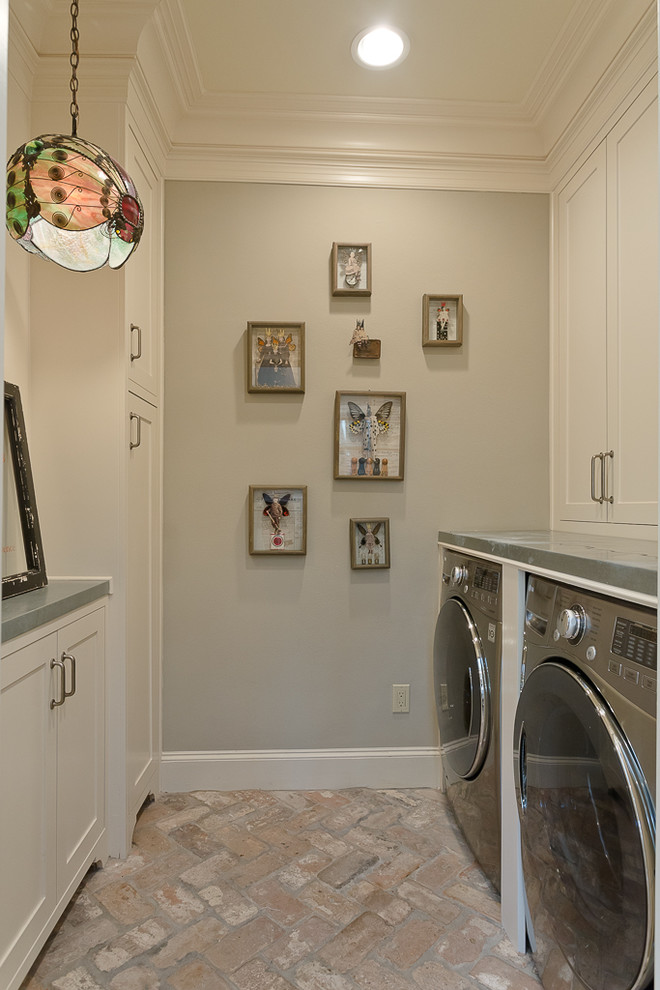 This is an example of a mid-sized transitional galley utility room in Houston with beige cabinets, zinc benchtops, grey walls, brick floors and a side-by-side washer and dryer.