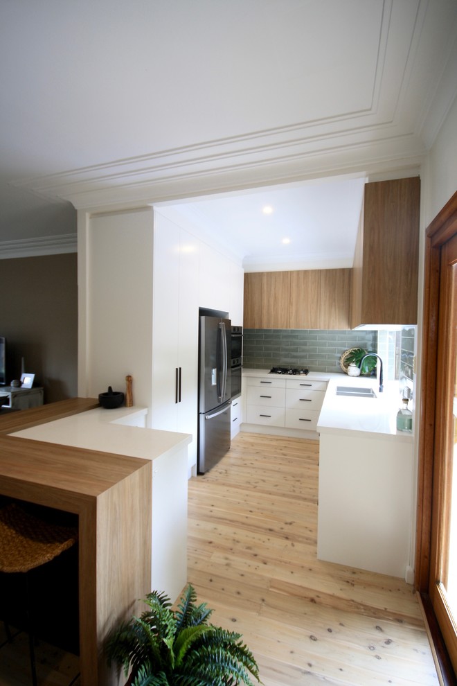 Photo of a mid-sized modern u-shaped open plan kitchen in Sydney with an undermount sink, flat-panel cabinets, white cabinets, quartz benchtops, green splashback, subway tile splashback, stainless steel appliances, medium hardwood floors, no island, brown floor and white benchtop.