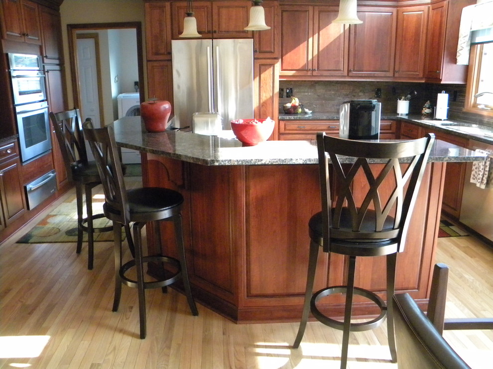 Example of a mid-sized transitional u-shaped light wood floor eat-in kitchen design with an undermount sink, raised-panel cabinets, medium tone wood cabinets, granite countertops, multicolored backsplash, stone tile backsplash, stainless steel appliances and an island