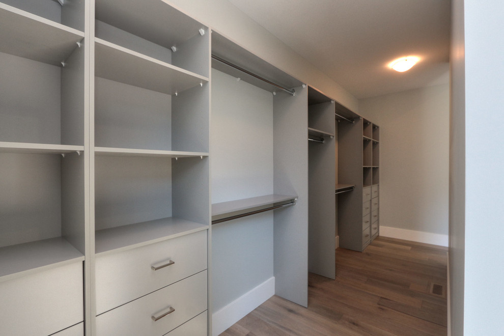 Large modern gender-neutral walk-in wardrobe in Other with flat-panel cabinets, grey cabinets, medium hardwood floors and brown floor.