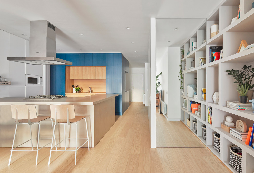 Design ideas for a contemporary u-shaped open plan kitchen in Barcelona with blue cabinets, white appliances, light hardwood floors, a peninsula, brown floor, beige benchtop, beige splashback, window splashback and flat-panel cabinets.