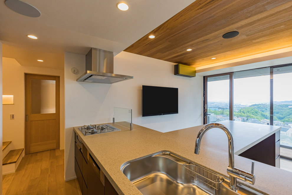 Bild på ett stort funkis grå grått kök och matrum, med bänkskiva i kvarts, ljust trägolv, en halv köksö och beiget golv