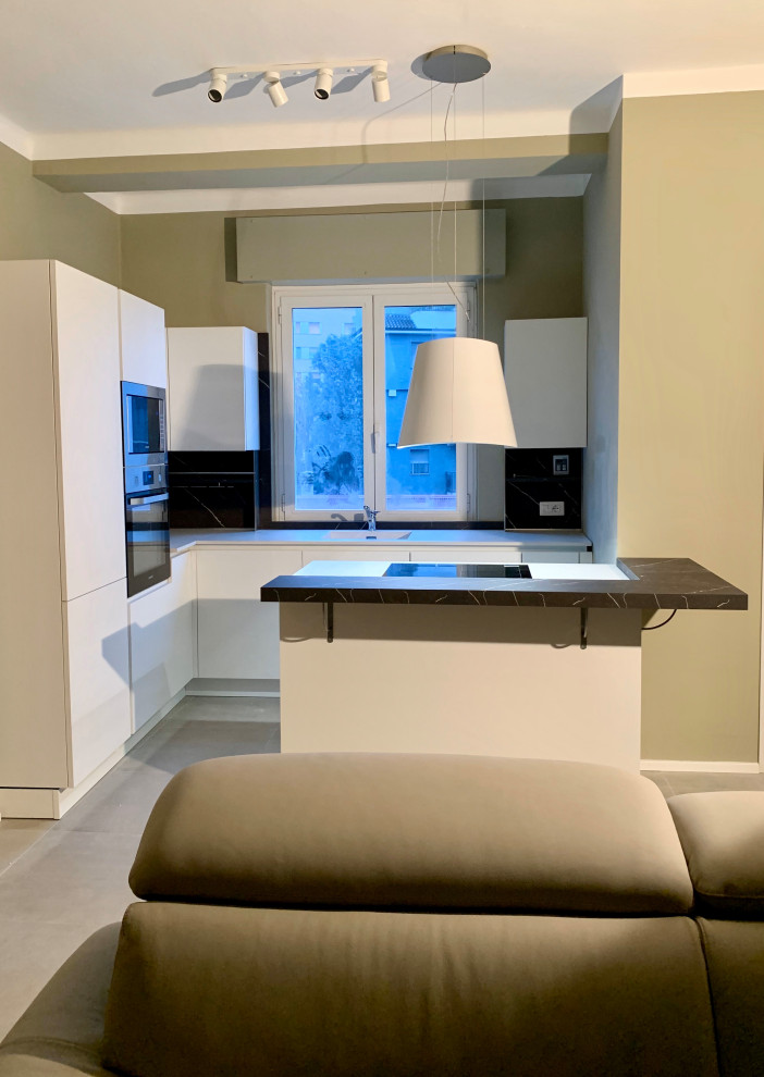 Photo of a small modern l-shaped open plan kitchen in Milan with a drop-in sink, flat-panel cabinets, white cabinets, stainless steel appliances, porcelain floors, with island, grey floor and brown benchtop.