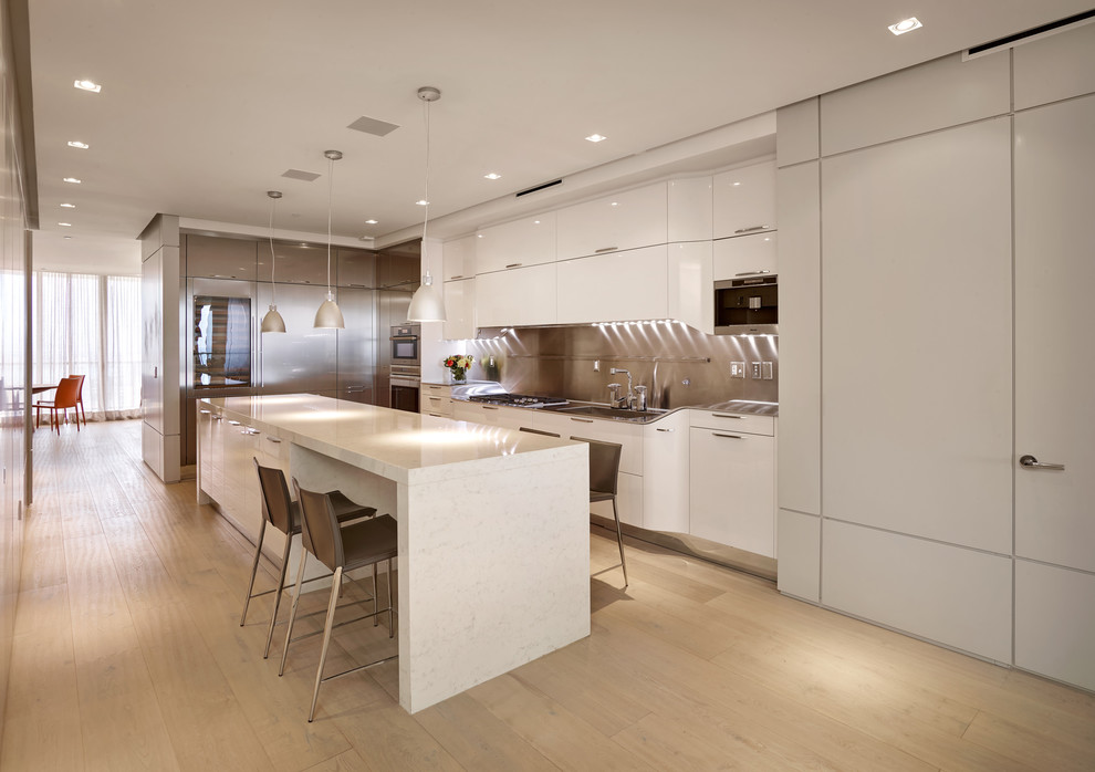 Inspiration for a large contemporary l-shaped kitchen in Miami with a single-bowl sink, flat-panel cabinets, white cabinets, marble benchtops, metallic splashback, metal splashback, stainless steel appliances, light hardwood floors and with island.