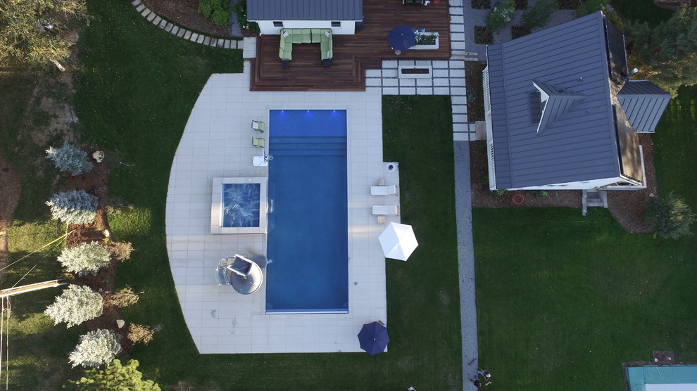 This is an example of an expansive country backyard rectangular lap pool in Denver with a hot tub and concrete pavers.