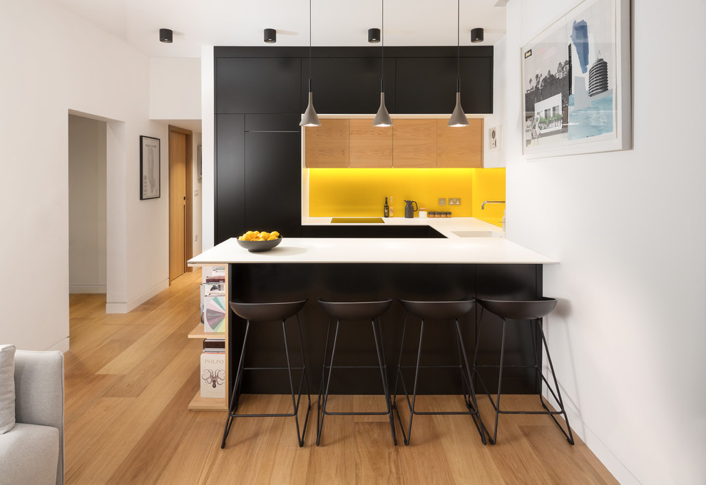 This is an example of a small contemporary u-shaped kitchen in London with an undermount sink, flat-panel cabinets, yellow splashback, light hardwood floors, a peninsula, brown floor and panelled appliances.