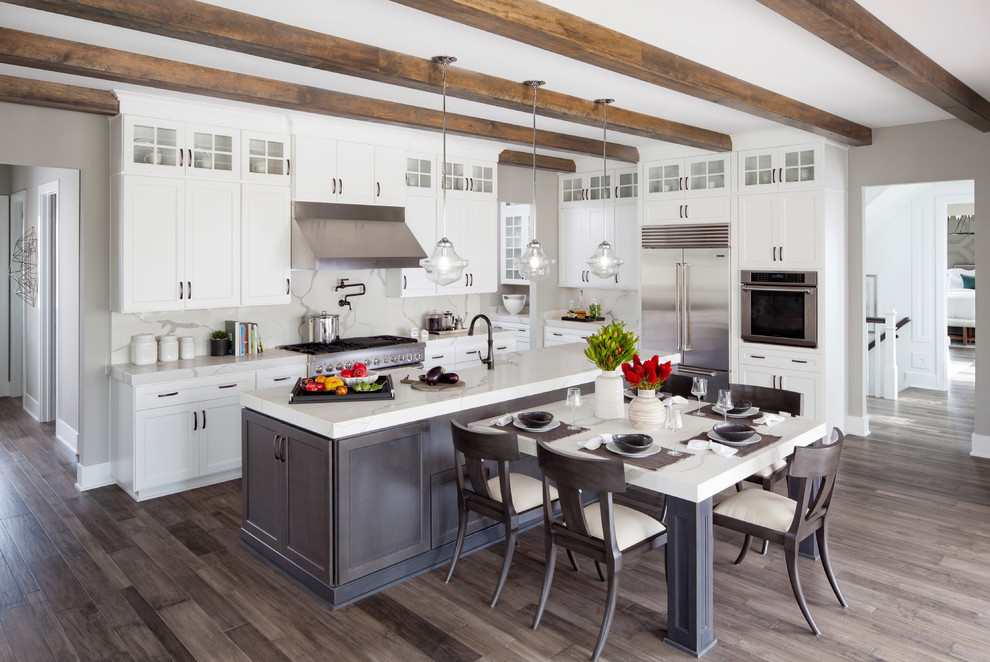 Photo of a transitional l-shaped eat-in kitchen in Denver with shaker cabinets, white cabinets, white splashback, stainless steel appliances, medium hardwood floors, with island, brown floor and white benchtop.