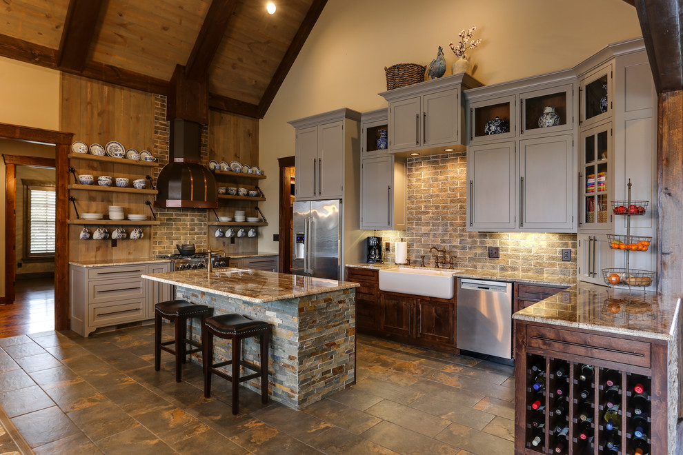 This is an example of a large country u-shaped kitchen in Raleigh with brown splashback, ceramic floors, with island, a farmhouse sink, beaded inset cabinets, grey cabinets, granite benchtops, stone tile splashback, stainless steel appliances and brown floor.