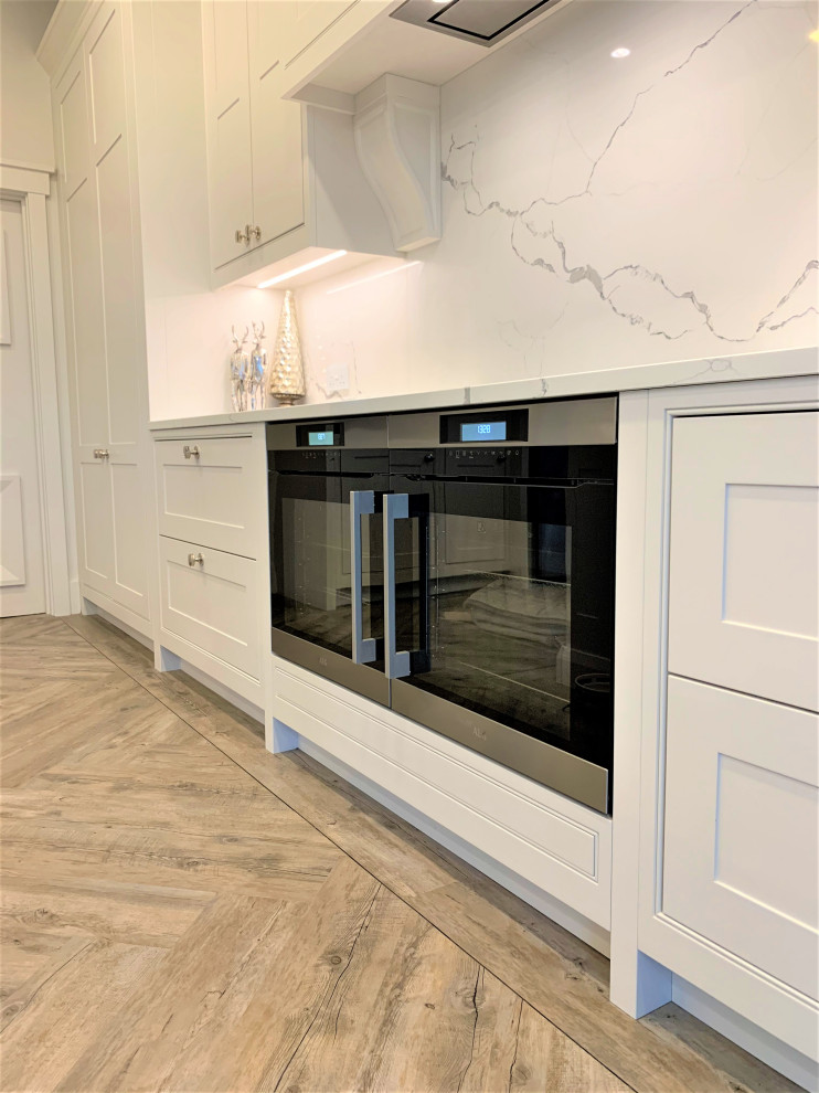 This is an example of a large classic l-shaped kitchen/diner in Other with a double-bowl sink, shaker cabinets, light wood cabinets, quartz worktops, white splashback, black appliances, vinyl flooring, an island and white worktops.