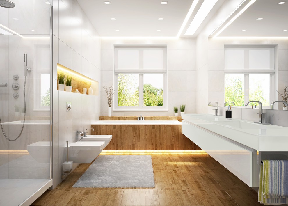 Inspiration for a large contemporary master bathroom in Portland with flat-panel cabinets, white cabinets, a drop-in tub, an alcove shower, a bidet, gray tile, white tile, stone slab, white walls, medium hardwood floors, an undermount sink, solid surface benchtops, brown floor and a hinged shower door.