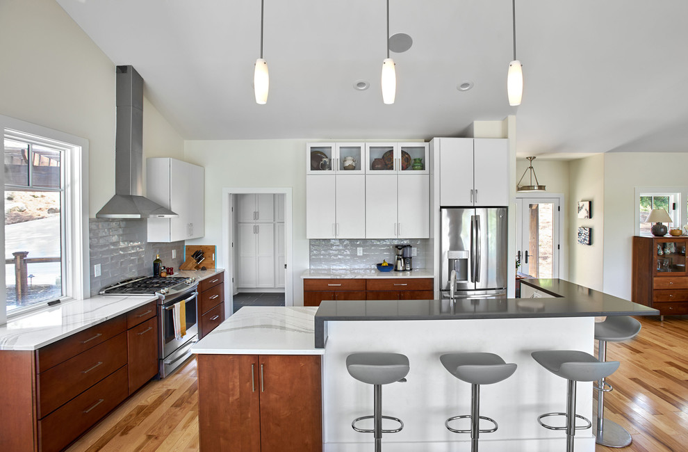 Mid-sized contemporary l-shaped open plan kitchen in Other with flat-panel cabinets, brown cabinets, grey splashback, stainless steel appliances, light hardwood floors, with island, white benchtop, marble benchtops and glass tile splashback.