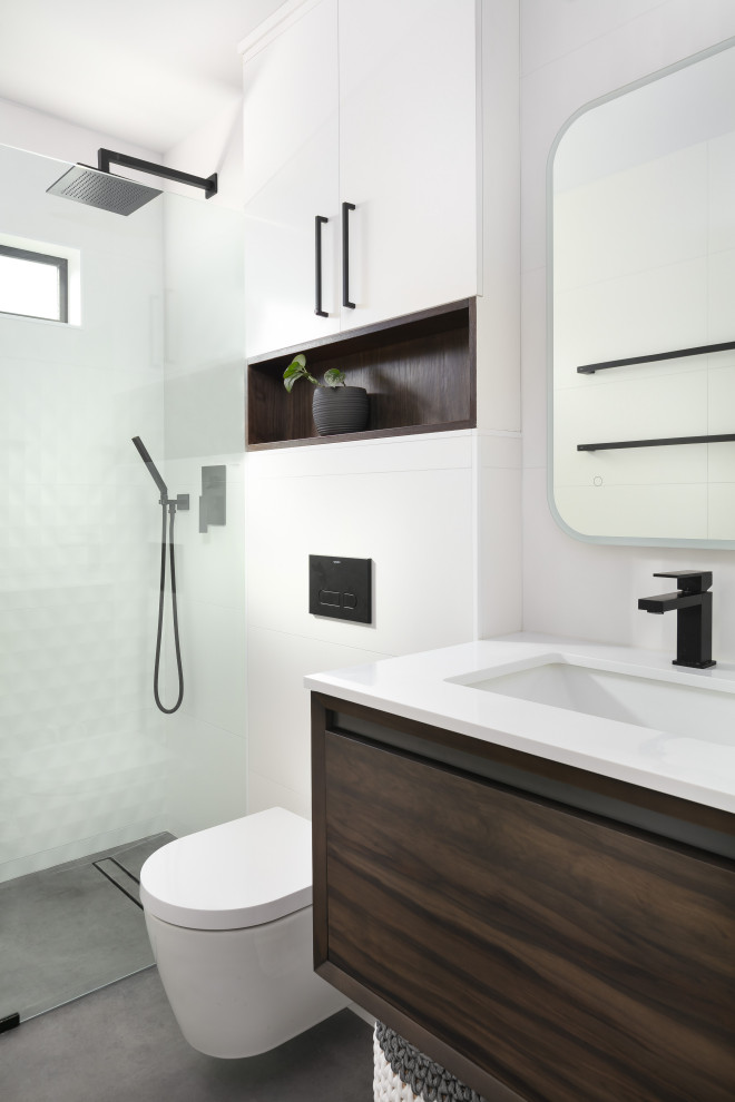 Modern inredning av ett litet vit vitt en-suite badrum, med släta luckor, skåp i mörkt trä, en kantlös dusch, en vägghängd toalettstol, vit kakel, porslinskakel, klinkergolv i porslin, ett undermonterad handfat, bänkskiva i kvarts, svart golv och med dusch som är öppen