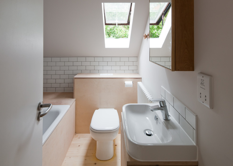 Mid-sized scandinavian 3/4 bathroom in Buckinghamshire with light wood cabinets, a drop-in tub, white tile, light hardwood floors, a one-piece toilet, ceramic tile, white walls, a console sink and beige floor.