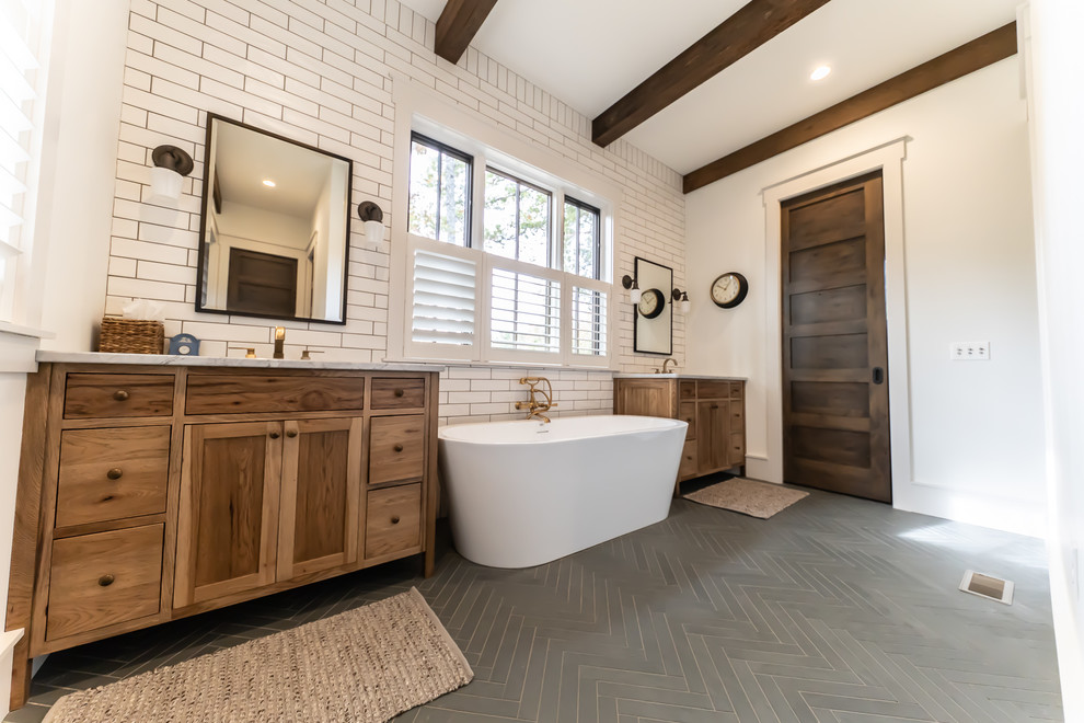 Inspiration for a country master bathroom in Other with furniture-like cabinets, medium wood cabinets, a freestanding tub, white tile, ceramic tile, white walls, slate floors, an undermount sink, marble benchtops, grey floor and white benchtops.