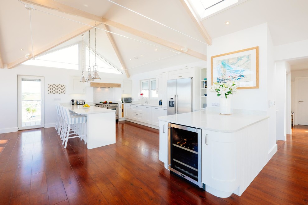 Photo of a beach style l-shaped open plan kitchen in Cornwall with shaker cabinets, white cabinets, stainless steel appliances, medium hardwood floors and a peninsula.