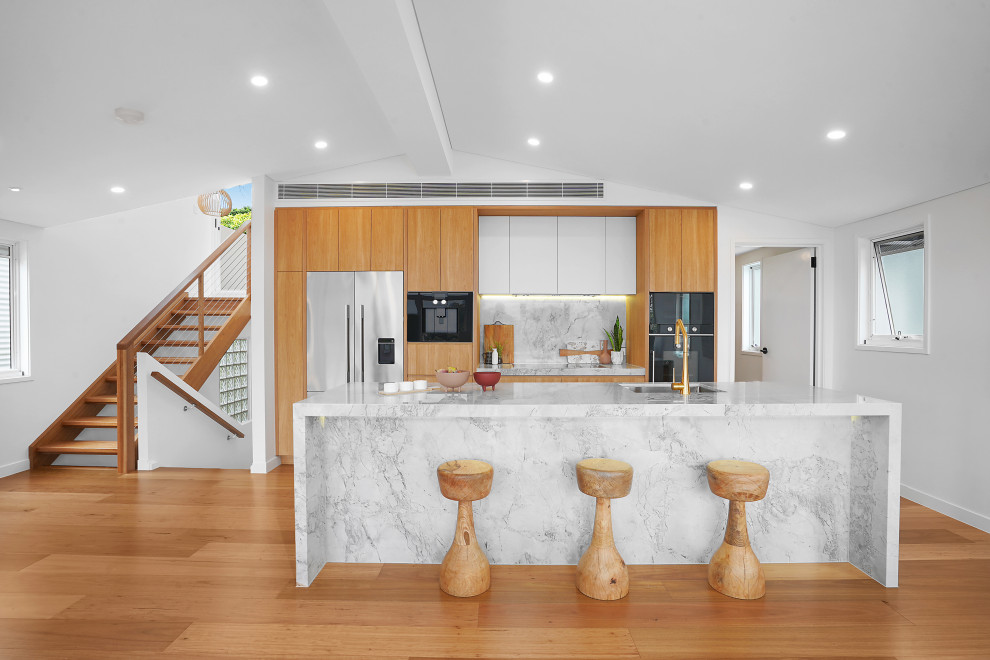 Inspiration for a large contemporary galley open plan kitchen in Brisbane with an undermount sink, flat-panel cabinets, medium wood cabinets, grey splashback, stainless steel appliances, with island, brown floor and grey benchtop.