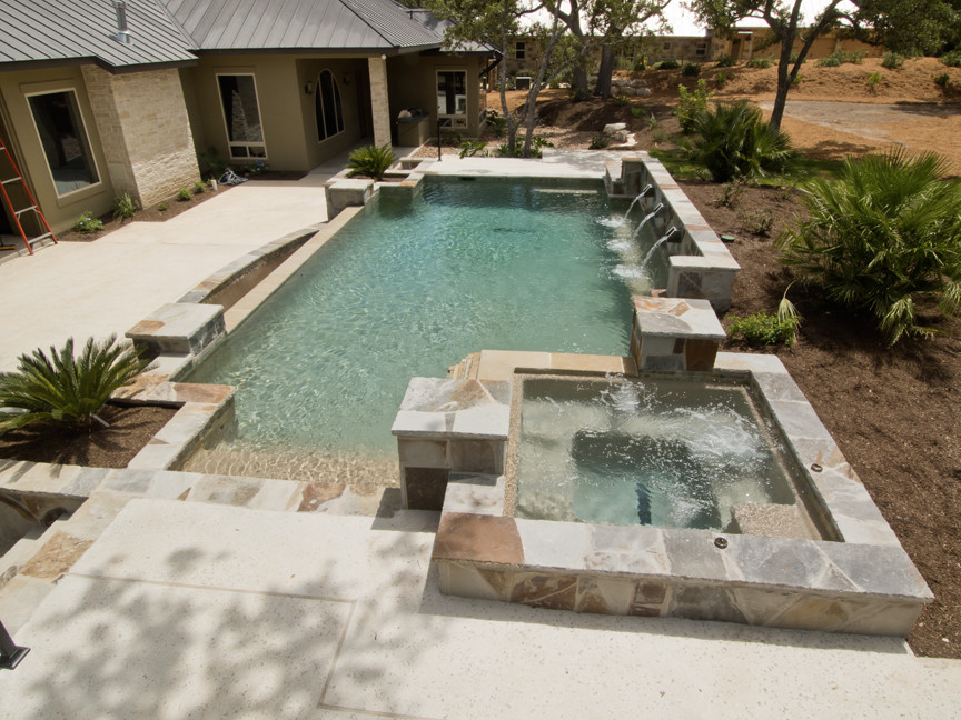 Inspiration for a mid-sized mediterranean backyard custom-shaped infinity pool in Austin with a hot tub and concrete slab.