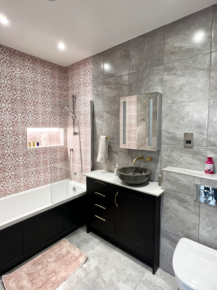 Photo of a contemporary grey and pink ensuite bathroom in London with brown cabinets, a built-in bath, a one-piece toilet, multi-coloured tiles, ceramic flooring, a built-in sink, grey floors, white worktops, a wall niche, a single sink and a freestanding vanity unit.
