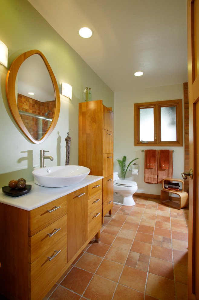 This is an example of a small contemporary bathroom in Sacramento with medium wood cabinets, a shower/bathtub combo, a one-piece toilet, beige tile, terra-cotta tile, green walls, terra-cotta floors, a vessel sink and granite benchtops.