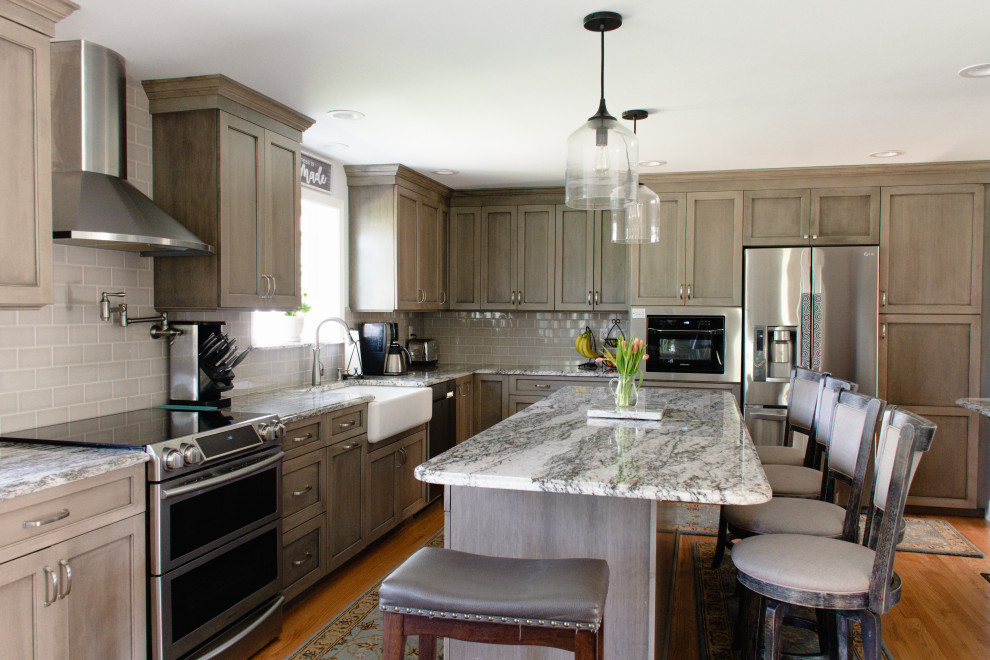 Inspiration for a large country l-shaped eat-in kitchen in Providence with a farmhouse sink, recessed-panel cabinets, medium wood cabinets, granite benchtops, beige splashback, ceramic splashback, stainless steel appliances, medium hardwood floors, with island, red floor and grey benchtop.