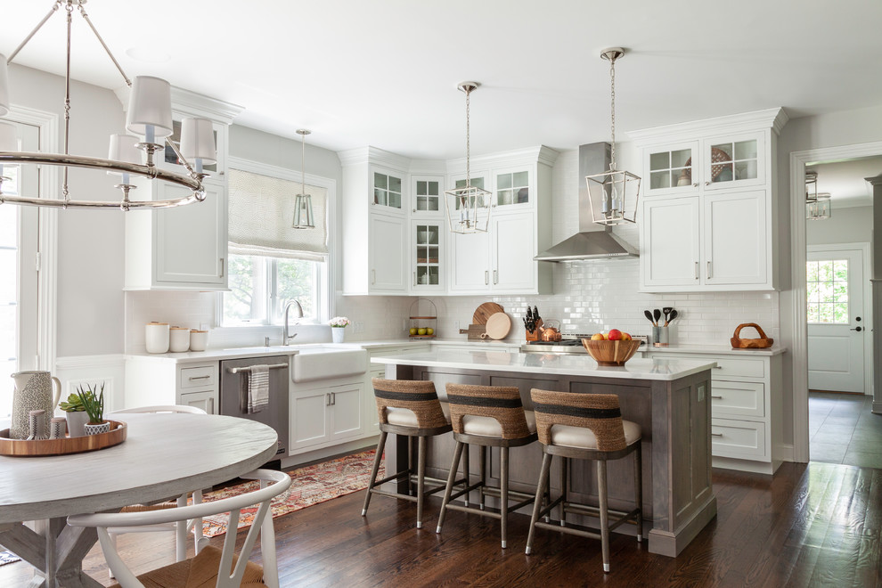 Design ideas for a transitional open plan kitchen in New York with a farmhouse sink, shaker cabinets, white cabinets, quartz benchtops, white splashback, ceramic splashback, stainless steel appliances, medium hardwood floors, with island and white benchtop.
