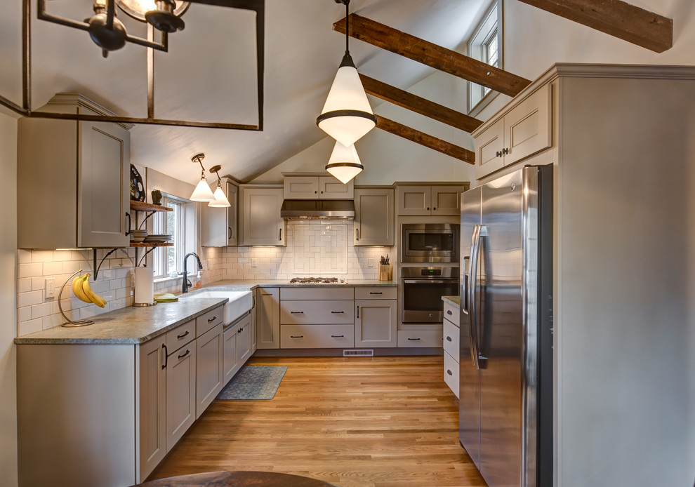Inspiration for a mid-sized traditional l-shaped kitchen in Boston with a farmhouse sink, recessed-panel cabinets, beige cabinets, granite benchtops, beige splashback, subway tile splashback, stainless steel appliances, medium hardwood floors, no island, brown floor and grey benchtop.