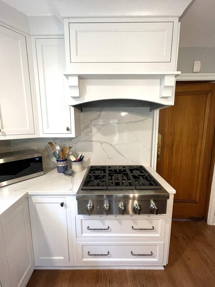 Medium sized traditional l-shaped kitchen/diner in Detroit with a submerged sink, shaker cabinets, white cabinets, engineered stone countertops, white splashback, engineered quartz splashback, stainless steel appliances, medium hardwood flooring, an island, brown floors and white worktops.