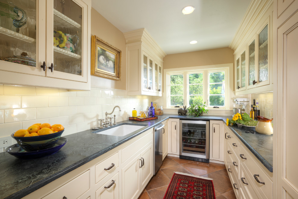 Design ideas for a mid-sized traditional u-shaped kitchen pantry in Sacramento with no island, recessed-panel cabinets, white cabinets, soapstone benchtops, white splashback, ceramic splashback, stainless steel appliances, a single-bowl sink and porcelain floors.