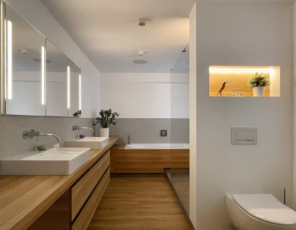 Идея дизайна: серо-белая ванная комната среднего размера в современном стиле с плоскими фасадами, светлыми деревянными фасадами, накладной ванной, открытым душем, инсталляцией, серой плиткой, белыми стенами, полом из винила, настольной раковиной, открытым душем, нишей, тумбой под две раковины и встроенной тумбой