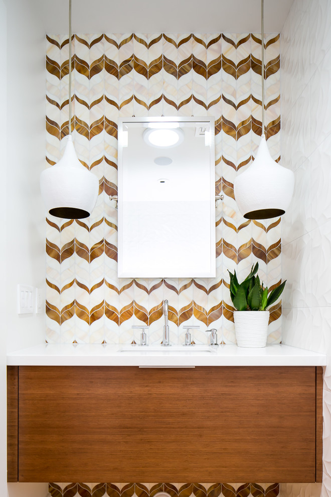 Photo of a midcentury powder room in Phoenix with medium wood cabinets, white tile, beige tile, brown tile, glass tile, white walls, quartzite benchtops, flat-panel cabinets, an undermount sink and white benchtops.