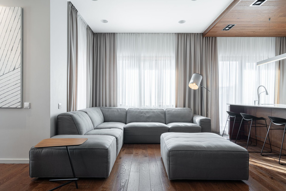Идея дизайна: большая гостиная комната в современном стиле с белыми стенами, темным паркетным полом, телевизором на стене и зоной отдыха