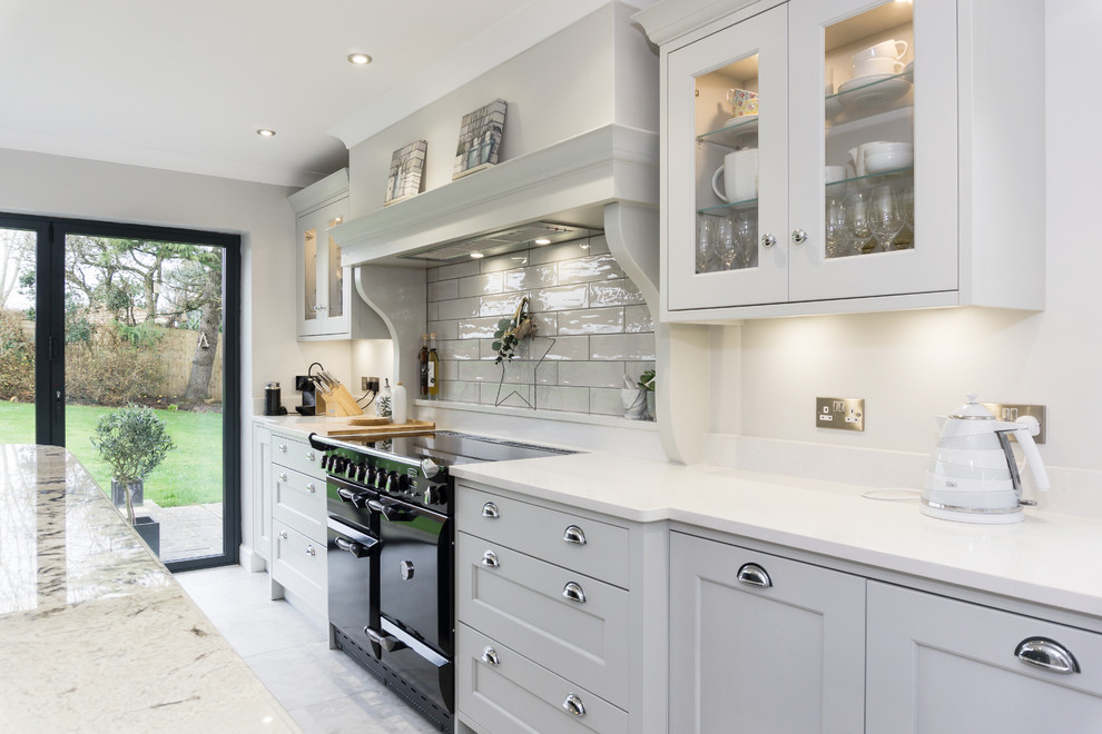 Large traditional grey and white single-wall kitchen/diner with a built-in sink, shaker cabinets, grey cabinets, engineered stone countertops, white splashback, ceramic splashback, black appliances, ceramic flooring, an island, grey floors and white worktops.