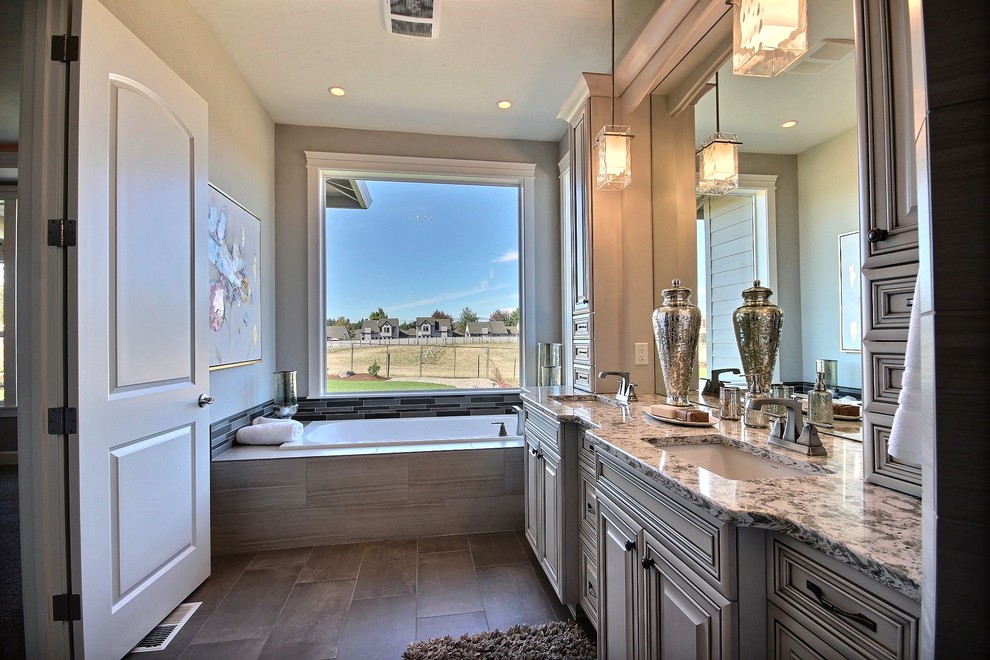 Inspiration for a mid-sized transitional master bathroom in Portland with raised-panel cabinets, medium wood cabinets, a drop-in tub, a curbless shower, a wall-mount toilet, gray tile, cement tile, grey walls, an undermount sink, engineered quartz benchtops and travertine floors.