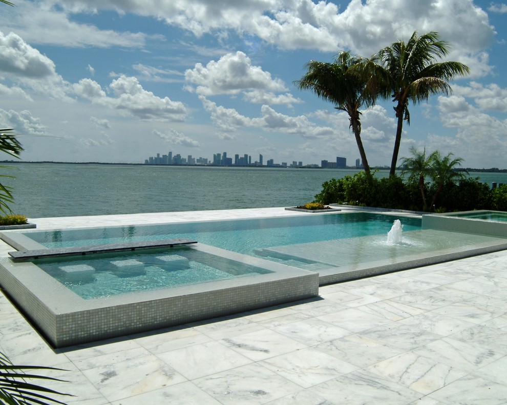 Design ideas for a tropical custom-shaped infinity pool with tile and a hot tub.
