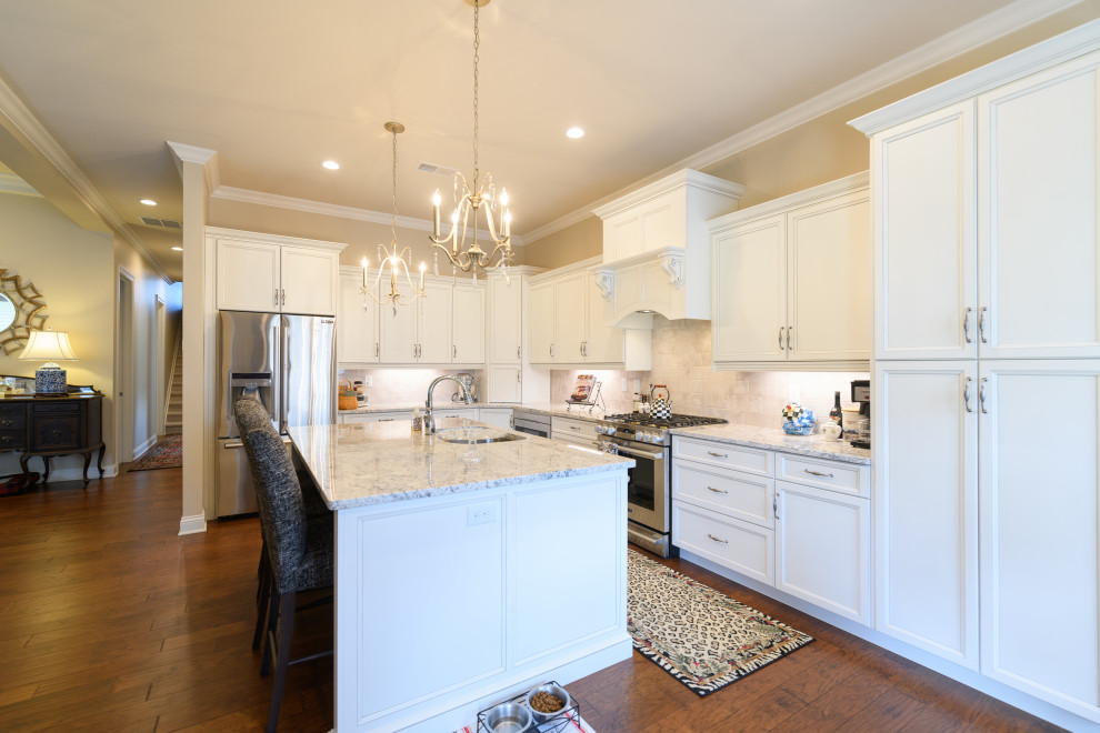 Example of a mid-sized transitional u-shaped dark wood floor and brown floor kitchen design with an undermount sink, shaker cabinets, white cabinets, granite countertops, beige backsplash, ceramic backsplash, stainless steel appliances, an island and white countertops