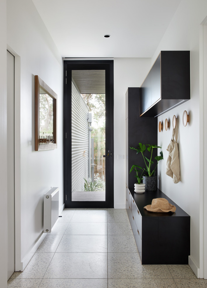 Cette image montre une entrée design de taille moyenne avec un vestiaire, un mur blanc, un sol en terrazzo et une porte noire.