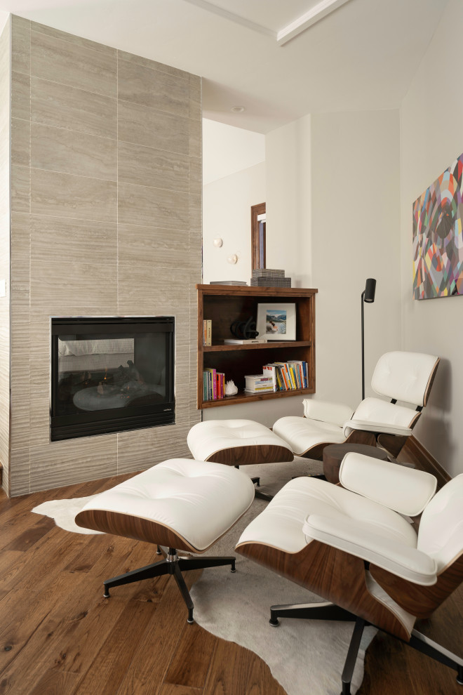 Idée de décoration pour une chambre parentale minimaliste avec un mur blanc, un sol en bois brun, une cheminée double-face et un manteau de cheminée en carrelage.