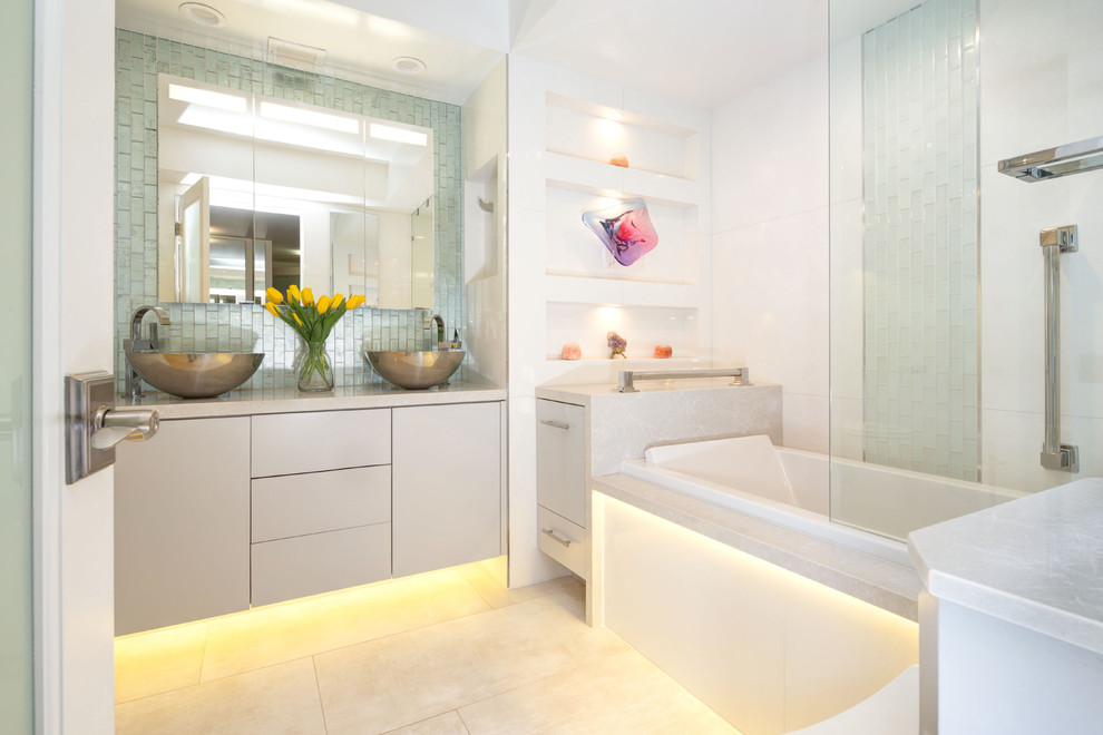 Design ideas for a mid-sized transitional bathroom in Los Angeles with flat-panel cabinets, an alcove tub, a shower/bathtub combo, a vessel sink, grey cabinets, a one-piece toilet, white tile, porcelain tile, porcelain floors, solid surface benchtops and a hinged shower door.