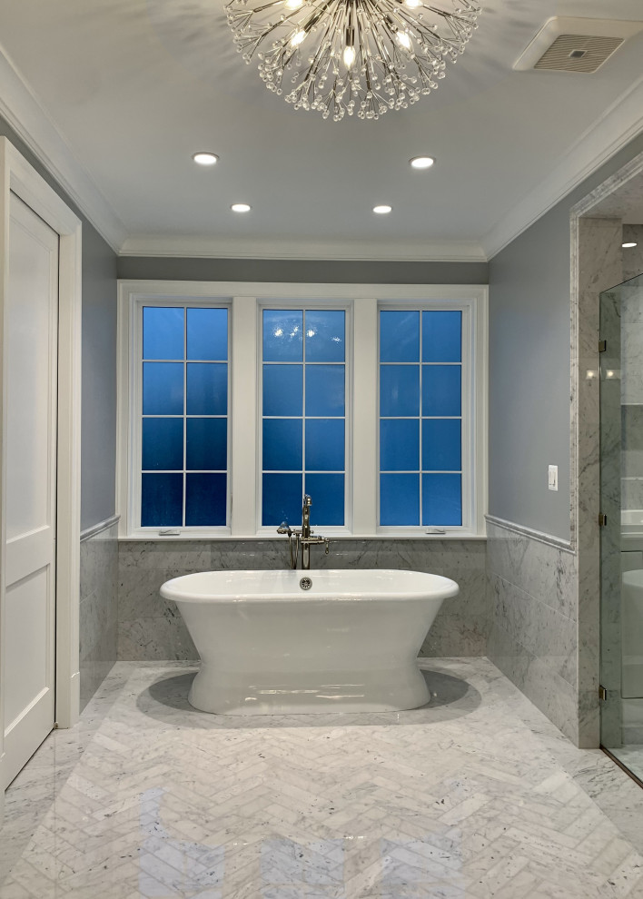 Пример оригинального дизайна: большая главная, серо-белая ванная комната в стиле неоклассика (современная классика) с фасадами с выступающей филенкой, синими фасадами, отдельно стоящей ванной, душевой комнатой, унитазом-моноблоком, серой плиткой, мраморной плиткой, серыми стенами, мраморным полом, врезной раковиной, мраморной столешницей, серым полом, душем с распашными дверями, белой столешницей, тумбой под две раковины и подвесной тумбой