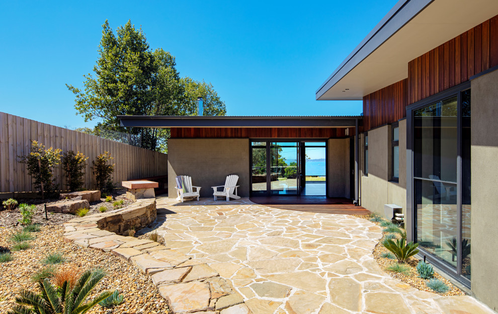 This is an example of a mid-sized midcentury backyard full sun xeriscape for summer in Melbourne with with rock feature and natural stone pavers.
