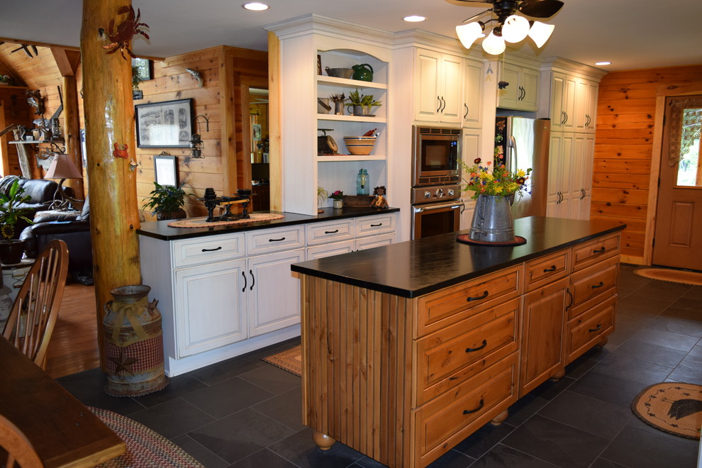 Large mountain style galley slate floor eat-in kitchen photo with a farmhouse sink, raised-panel cabinets, white cabinets, soapstone countertops, stainless steel appliances and an island