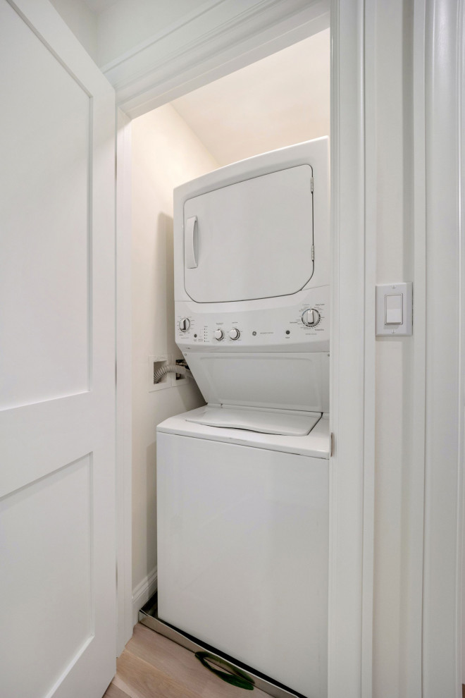 Foto di una lavanderia minimal con pareti bianche, parquet chiaro e lavatrice e asciugatrice a colonna