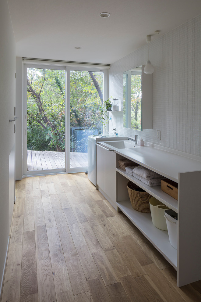 Inspiration for a modern single-wall laundry room in Other with an integrated sink, open cabinets, white cabinets, white walls, medium hardwood floors, brown floor and white benchtop.