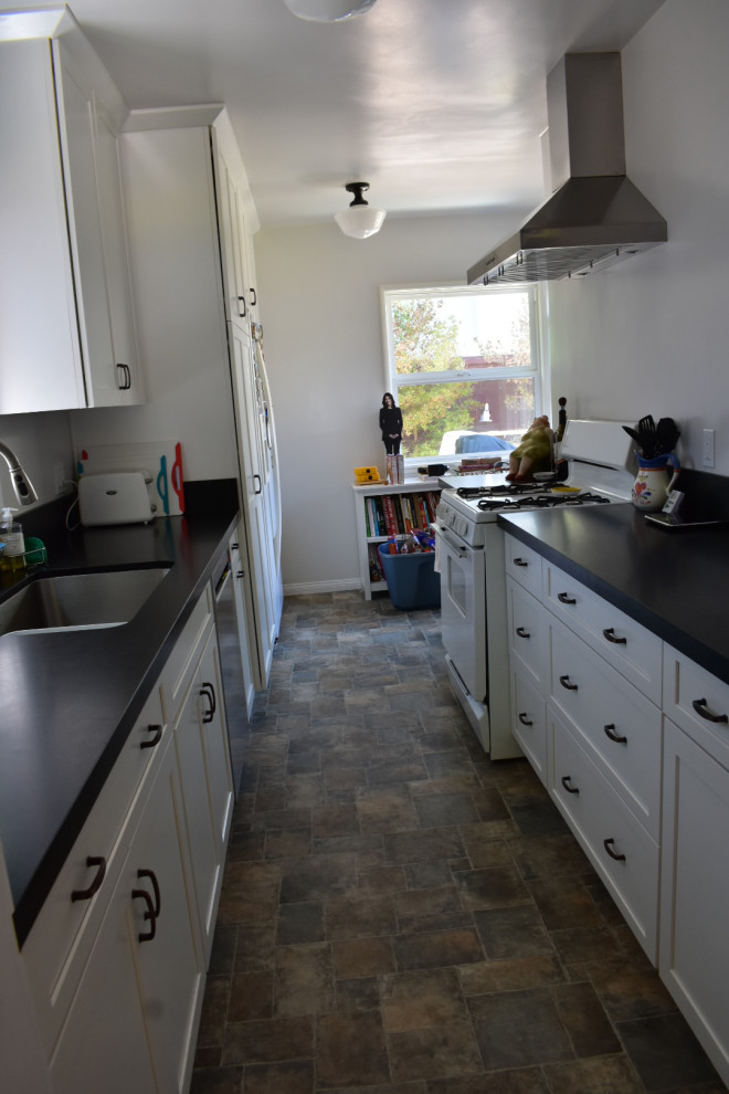 Photo of a mid-sized contemporary galley eat-in kitchen in Los Angeles with a single-bowl sink, shaker cabinets, white cabinets, solid surface benchtops, black splashback, engineered quartz splashback, stainless steel appliances, ceramic floors, no island, multi-coloured floor and black benchtop.