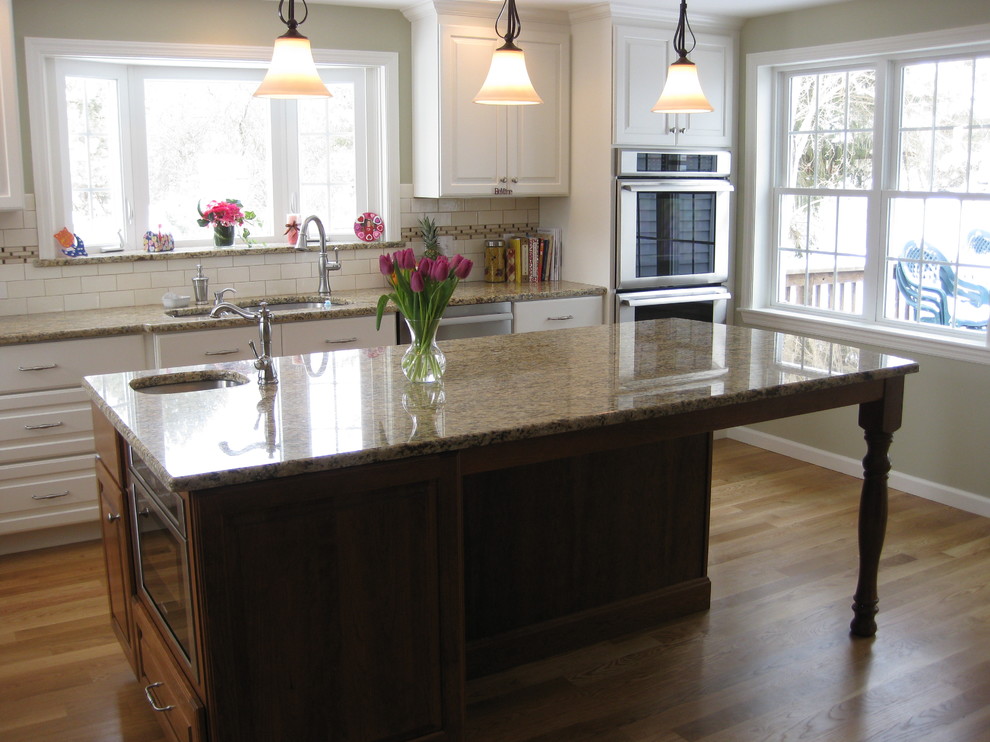 Transitional u-shaped medium tone wood floor eat-in kitchen photo in Boston with an undermount sink, raised-panel cabinets, white cabinets, granite countertops, white backsplash, ceramic backsplash, stainless steel appliances, an island and beige countertops