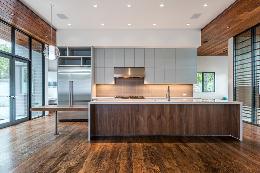 This is an example of a large contemporary galley eat-in kitchen in Houston with a single-bowl sink, flat-panel cabinets, grey cabinets, solid surface benchtops, brown splashback, glass tile splashback, stainless steel appliances, medium hardwood floors and with island.